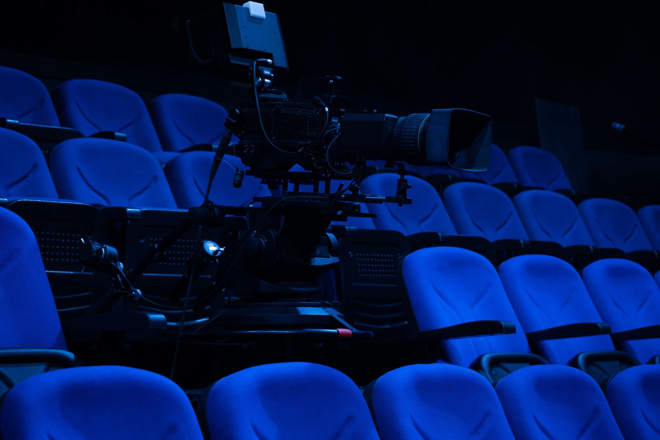 Professional broadcast camera in a blue-lit auditorium ready for live coverage